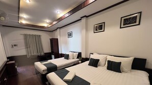 A hotel room with two beds, a small desk, a chair, a radiator, and a window with curtains. - La MaiSon Du laos Hotel (Luang Prabang)