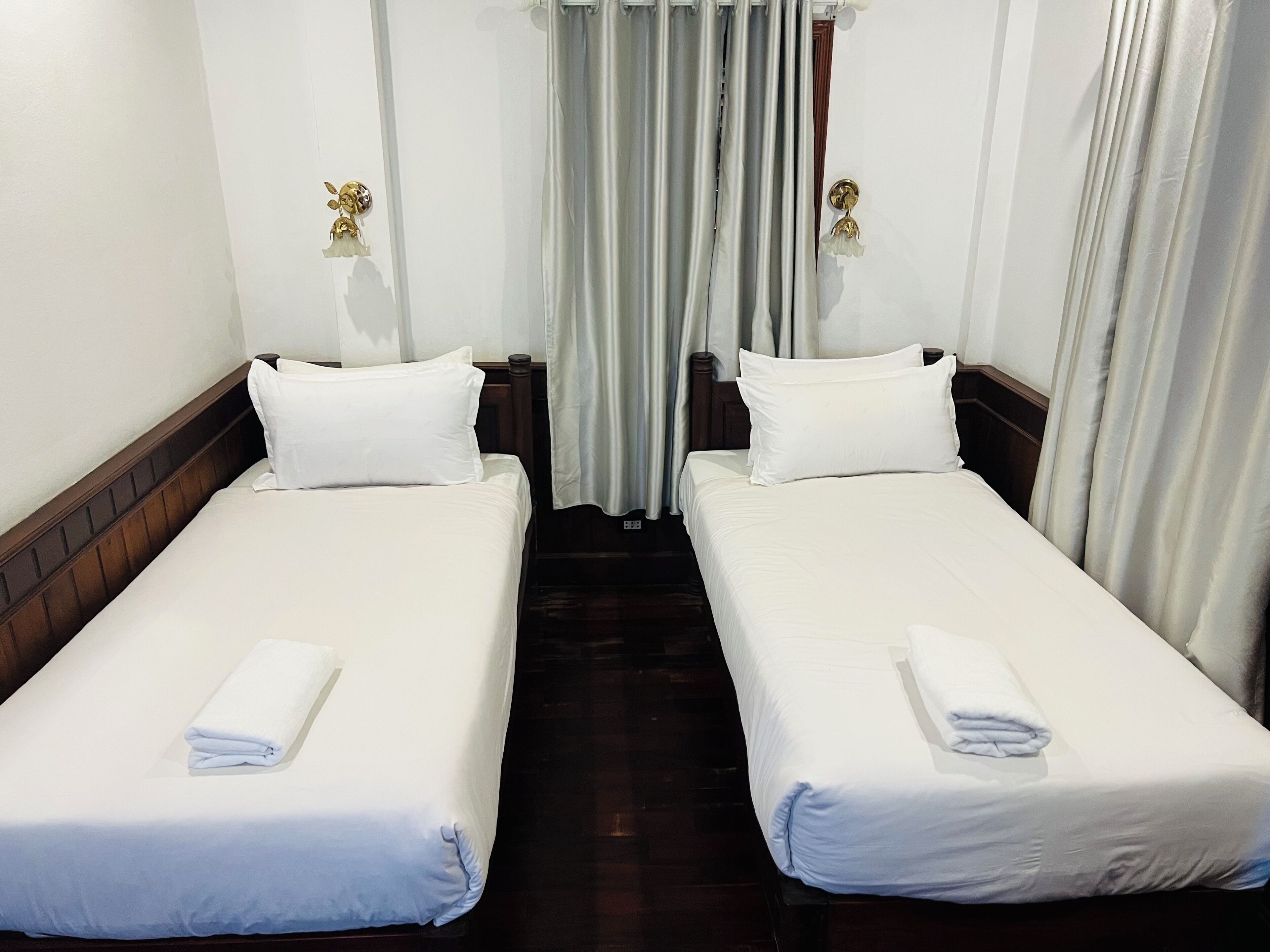 Habitación de hotel con dos camas individuales, ropa de cama blanca, cabecero de madera y una cortina.