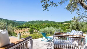 A wooden deck with a view of a lush valley, a blue chair, and a white sofa. - Villa with private pool, hot tub. Quiet area & 100% privacy. panoramic views! (Umbria)