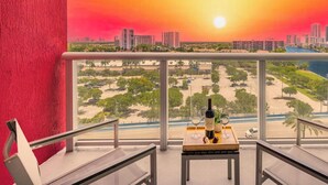Un balcone con vista sulla città al tramonto, un tavolo con bottiglia e bicchieri, e una sedia.