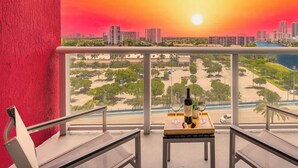 A balcony with a cityscape view at sunset, a table with a bottle and glasses, and a chair. - Spectacular Studio with pool and Amenities (Hallandale Beach)