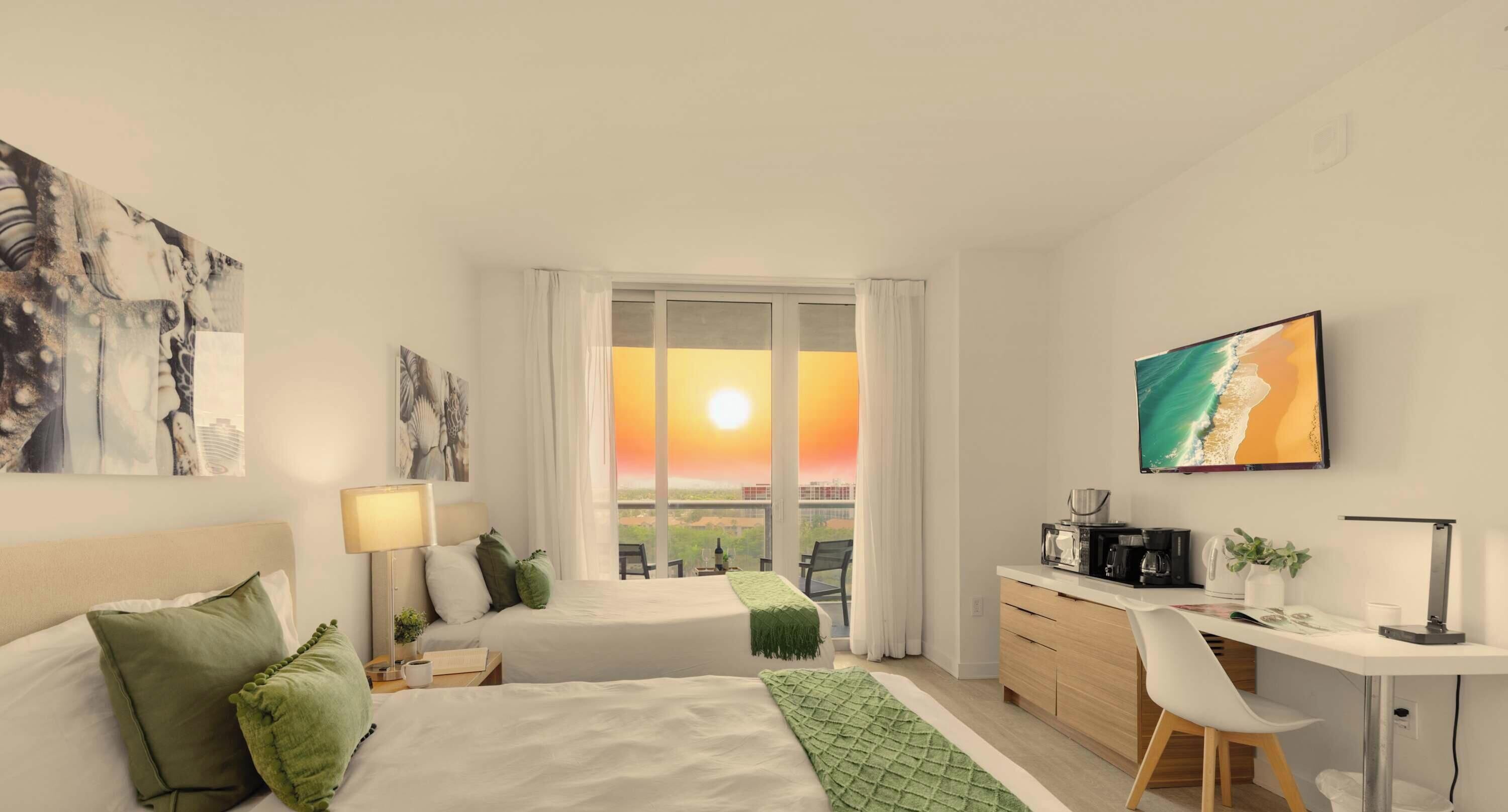A hotel room with two beds, a desk, a chair, a coffee machine, and a large window with a sunset view.