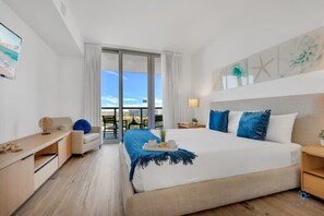 Quarto de hotel moderno com uma cama grande, uma escrivaninha, uma cadeira e uma varanda com vista para a cidade.