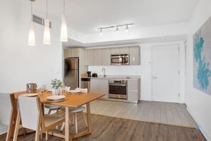 Cozinha moderna com eletrodomésticos de aço inoxidável, sala de jantar com mesa e cadeiras de madeira, e esquema de cores em branco.