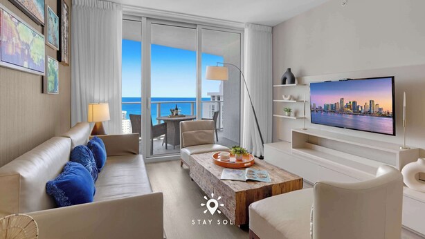 Ein modernes Hotelzimmer mit großem Balkon, einem Flachbildfernseher, einer Couch, einem Couchtisch und Meerblick.