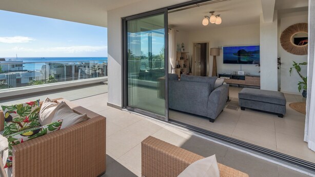 Een balkon met een rieten bank, een grijze bank en een televisie op de achtergrond.