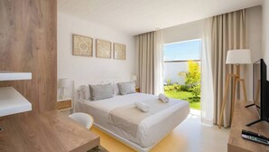 A modern hotel room with a large bed, a desk, a TV, and a view of a garden. - Villa BIJOU, 3 bed, grand bay center by Immoclair (Rivière du Rempart District)