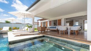 A modern outdoor pool area with lounge chairs and umbrellas, a wooden deck, and a seating area with a table and chairs. - Villa BIJOU, 3 bed, grand bay center by Immoclair (Rivière du Rempart District)