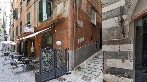 A narrow street with outdoor seating and a building with a sign for 'Al Giardino'. - Libeccio - Style and Comfort at Two Steps from the Cathedral (Genova)