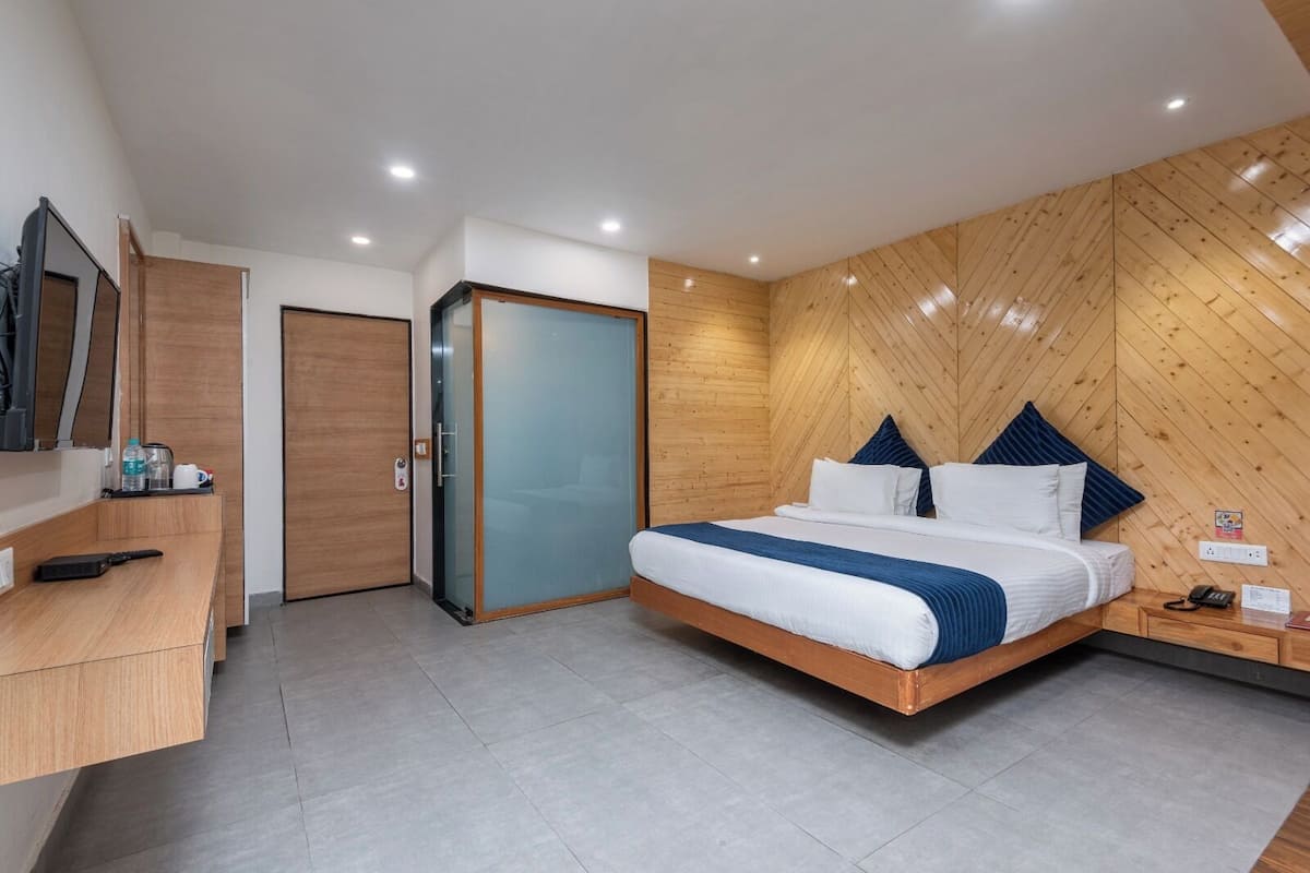 A modern bedroom with a large bed, a wooden wardrobe, a desk with a mirror, and a flat-screen TV.