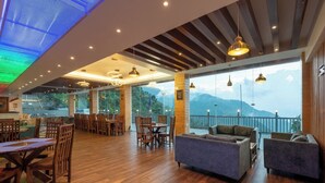 A spacious restaurant with wooden flooring, modern pendant lighting, and a view of mountains through large windows. - MV Acosta by Lawrence hotels (Mussoorie)