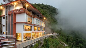 A hotel with a restaurant on the ground floor, multiple balconies, and a view of a forested hillside. - MV Acosta by Lawrence hotels (Mussoorie)