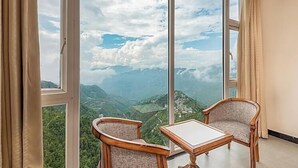 A room with a large window offering a mountain view. There are two chairs and a small table. - MV Acosta by Lawrence hotels (Mussoorie)