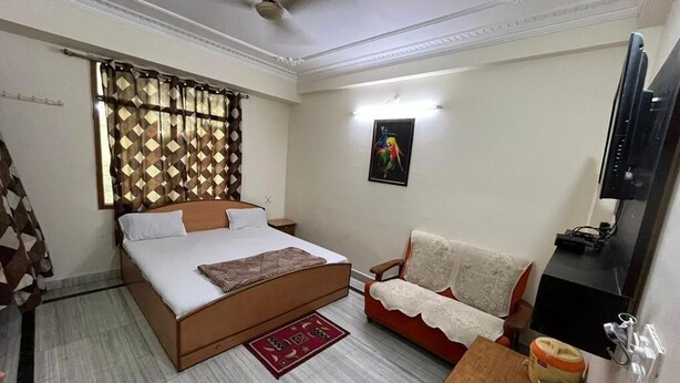 A bedroom with a bed, a sofa, a small table, and a television. - Giriraj kripa (Vrindavan)
