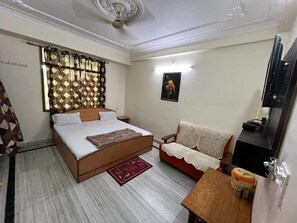 A bedroom with a bed, a sofa, a small table, and a television.