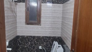 A small bathroom with a toilet, a shower, and a fan. - Giriraj kripa (Vrindavan)