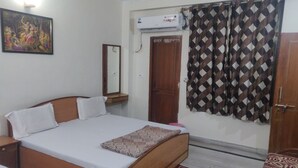 A bedroom with a bed, a mirror, an air conditioning unit, and a patterned curtain. - Giriraj kripa (Vrindavan)