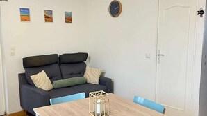 A modern living room with a dark grey sofa, light blue chairs, a wooden table, and a white door. - La maison d'Oscar, 200m plage (Asnelles)