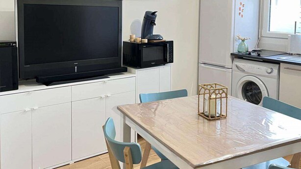 A compact kitchen with white cabinetry, a flat-screen TV, a microwave, and a washing machine. - La maison d'Oscar, 200m plage (Asnelles)