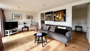 A living room with a grey sofa, a black coffee table, a TV on a white stand, and artwork on the walls.