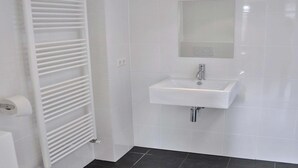 A bathroom with a white tiled wall, a white sink, a mirror, and a white towel rack.