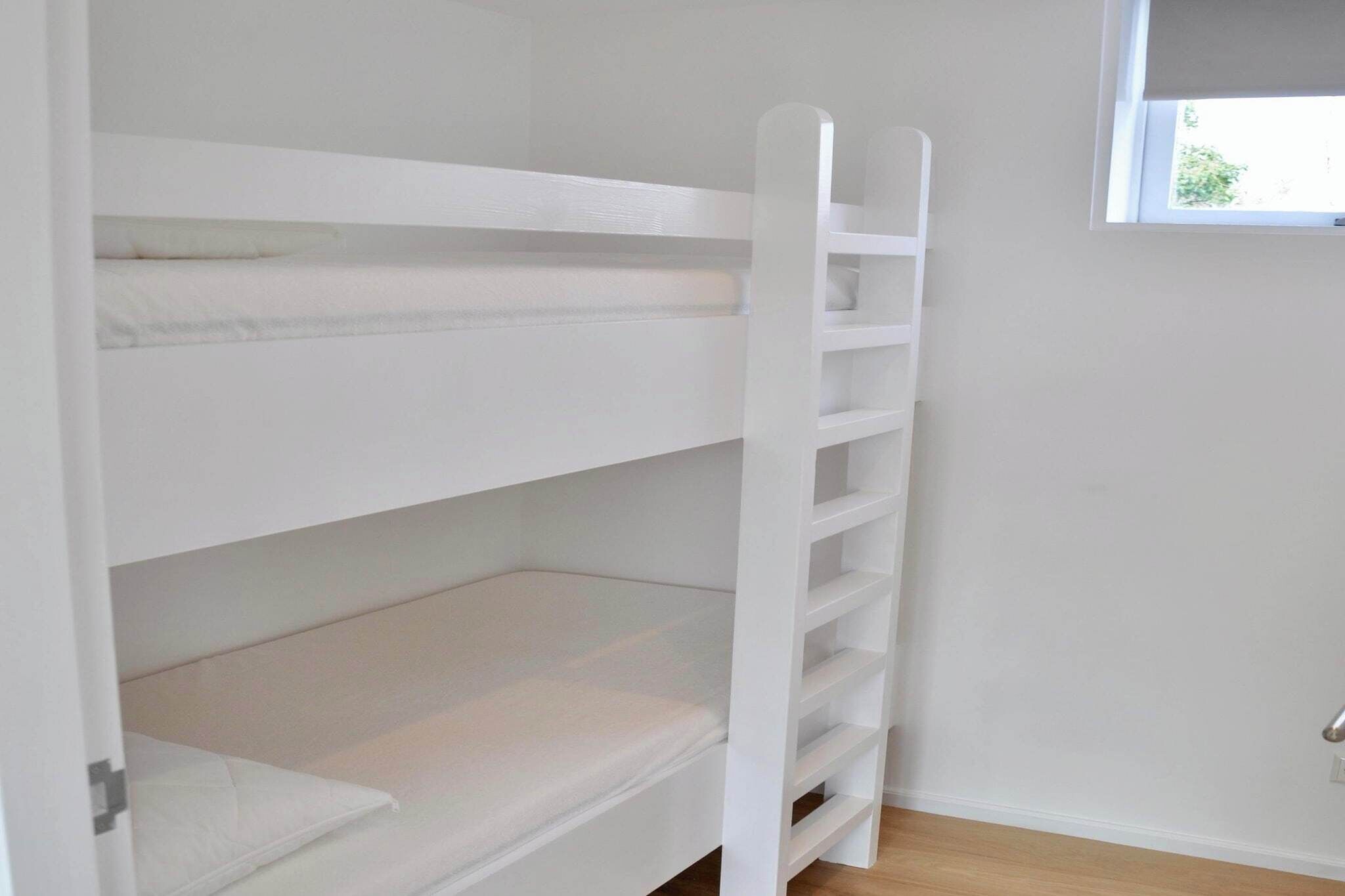 A bunk bed with a ladder, white walls, and a window.