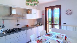 A modern kitchen with white cabinets, a gas stove, and a dining area with a table set for four. - House in Luino with Green Garden and City Views (Luino)