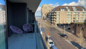 A balcony with two purple chairs, a view of a city street, and modern buildings in the background. - Apartment in Nieuwpoort near Marina (Nieuwpoort)