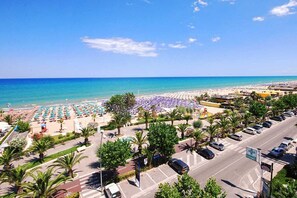 A beach with rows of umbrellas and sun loungers, a parking area, and a pharmacy sign.