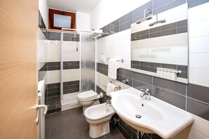 A bathroom with a shower, toilet, bidet, and two sinks.