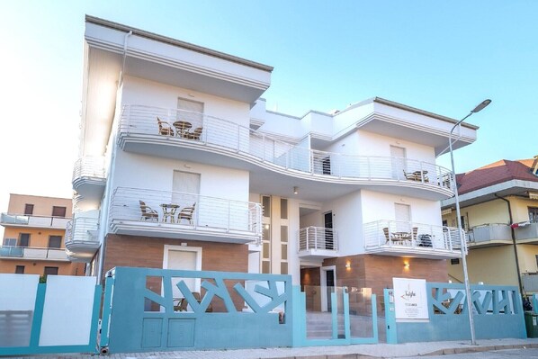 A multi-story residential building with balconies, a gated entrance, and a sign indicating a residential area.