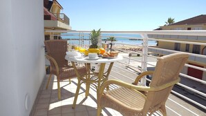 A balcony with wicker chairs, a round table, and a view of the beach.