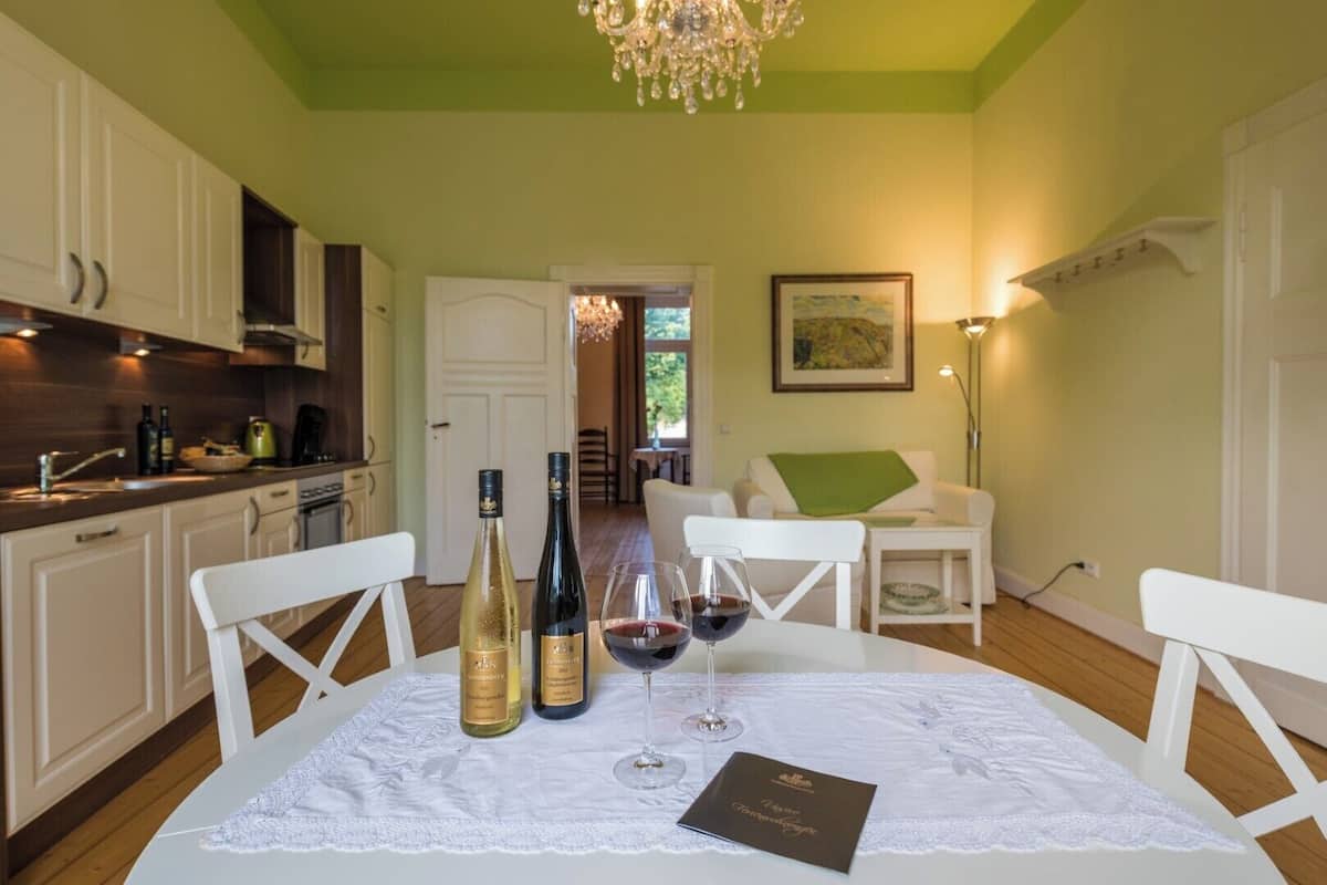 Un comedor con una mesa dispuesta para dos personas, que incluye una botella de vino y copas.