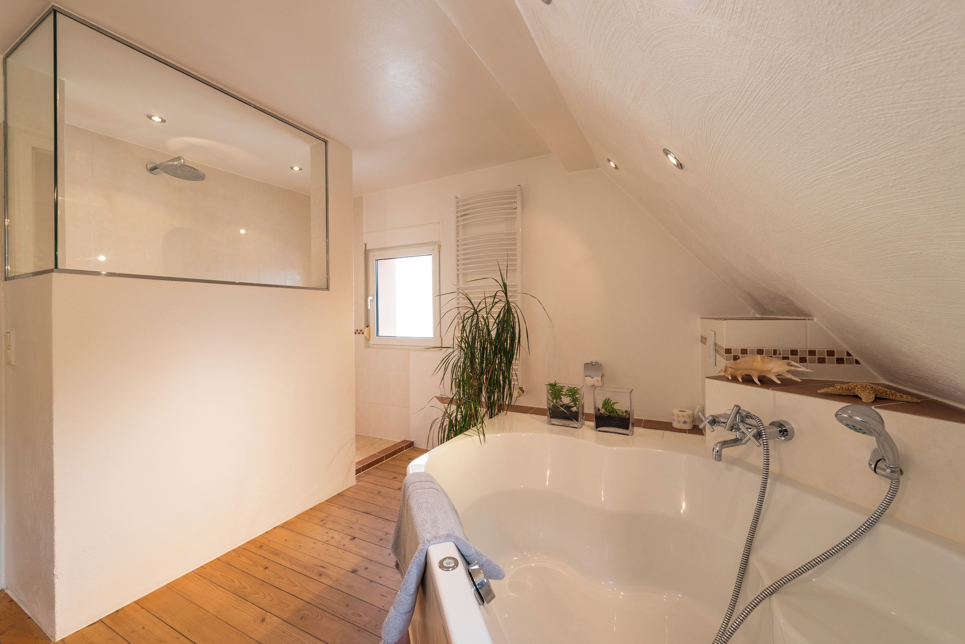 A modern bathroom with a freestanding bathtub, a glass shower enclosure, and a wooden floor.
