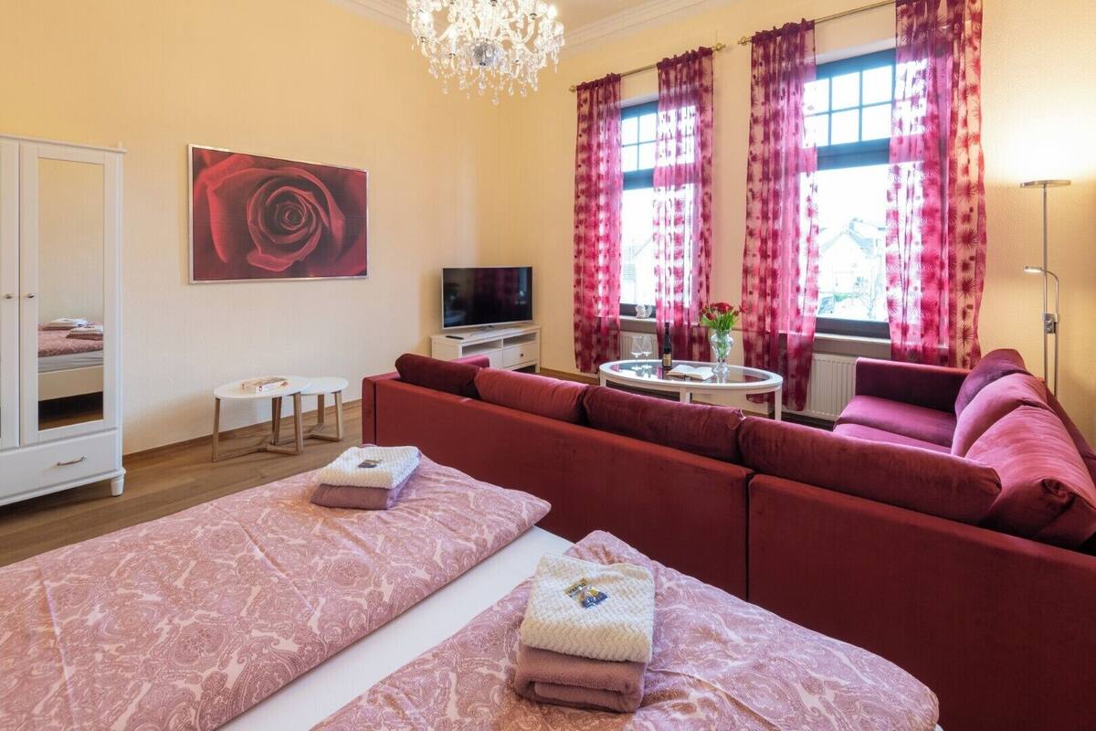 Una habitación de hotel con una cama grande, un sofá, un televisor, una mesita pequeña y un candelabro.