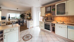 Une cuisine spacieuse avec des meubles blancs, un îlot central et un coin repas offrant une vue agréable.