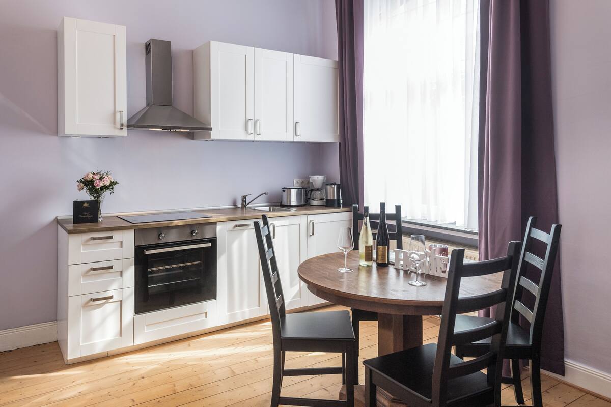 Una cocina moderna con armarios blancos, horno empotrado y comedor con mesa redonda y sillas.