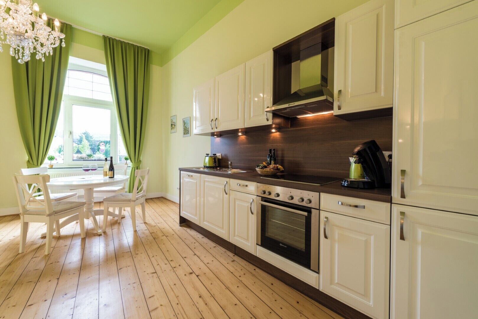 Een keuken met witte kasten, een ingebouwde oven en een eethoek met een tafel en stoelen.