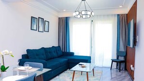 A modern living room with a blue sofa, a glass coffee table, and a dining area with a white table and chairs. - Staroot Residences- Celestial Chalet (Nairobi)