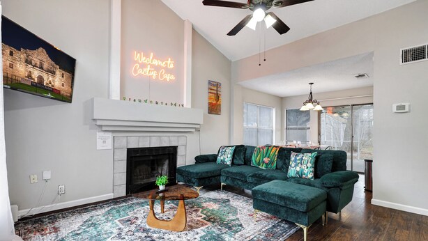 A living room with a sectional sofa, a fireplace, a ceiling fan, and a large window.