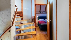Un estrecho pasillo con escaleras de madera que conducen a un dormitorio tipo loft con literas.
