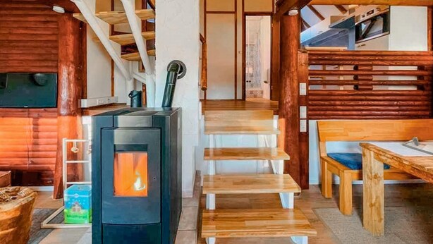 Un acogedor interior de cabaña con estufa de leña, una escalera y una zona de comedor.