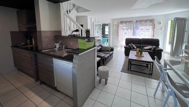 A modern kitchen with a built-in dishwasher, a dining area with a table and chairs, and a living room with a sofa and a TV.