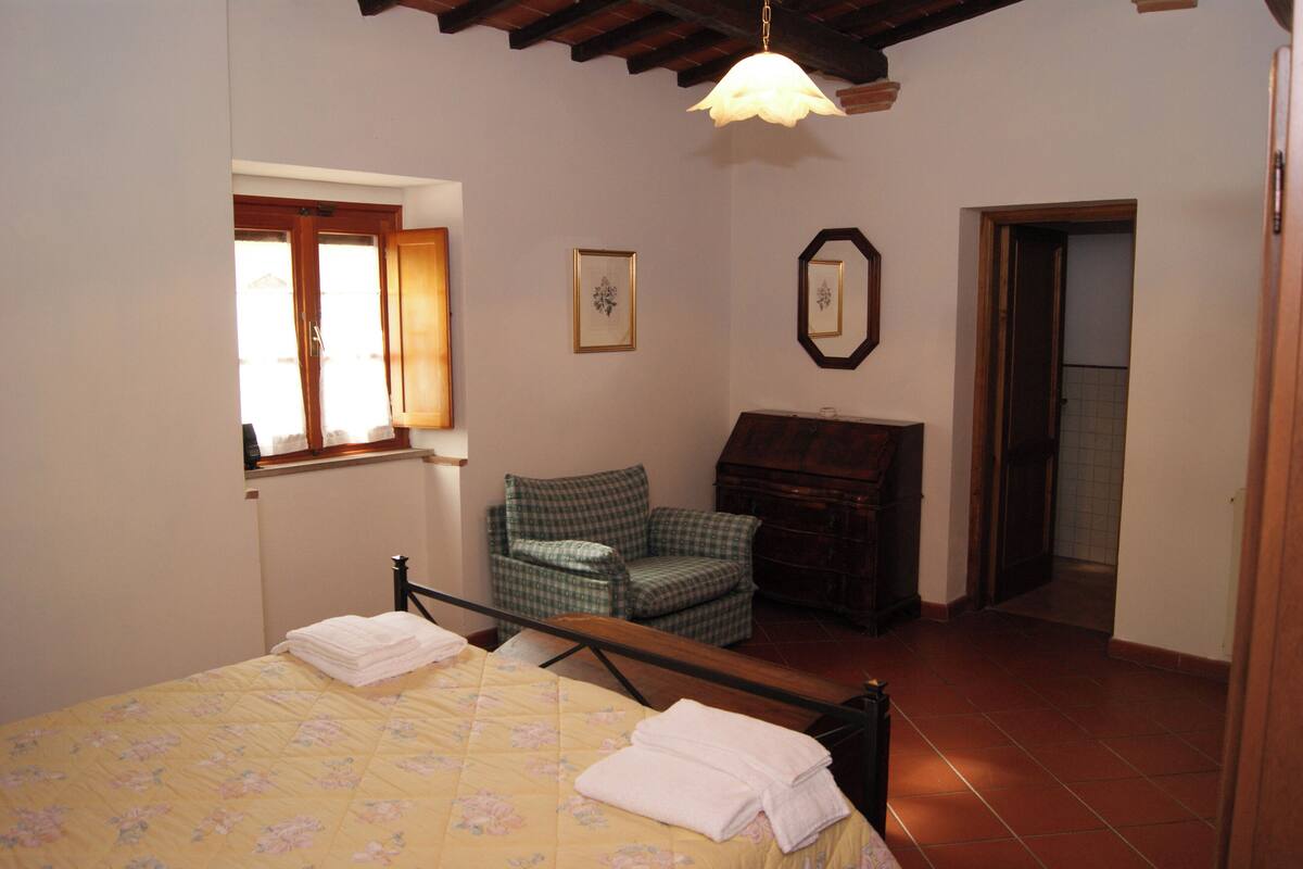 Un dormitorio con cama, una silla, un escritorio y una puerta que da a otra habitación.