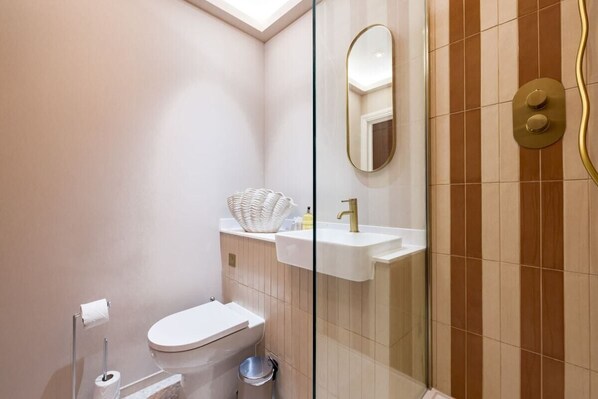 A modern bathroom with a toilet, sink, and glass shower enclosure. - The Belsize Park Escape - Modern 2bdr Apartment (London)