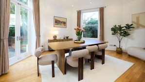 A dining area with a wooden table, six chairs, a vase with flowers, and a view of greenery outside. - The Hampstead Getaway - Charming 5bdr Home With Conservatory (London)
