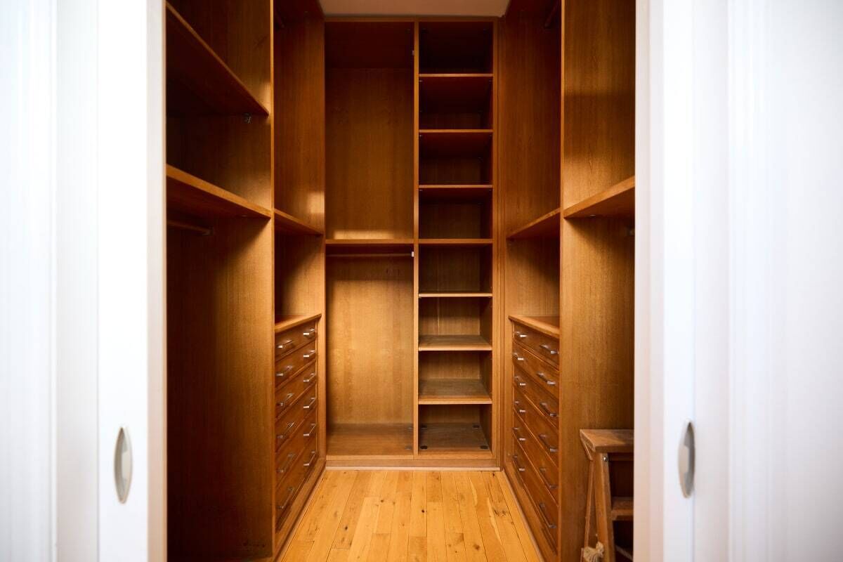 Un vestidor amplio con estantes y cajones, suelo de madera y paredes blancas.