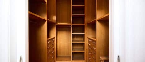 Un vestidor amplio con estantes y cajones, suelo de madera y paredes blancas.