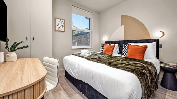 Un dormitorio moderno con una cama grande, un escritorio de madera y una ventana con vista a un edificio de ladrillo.