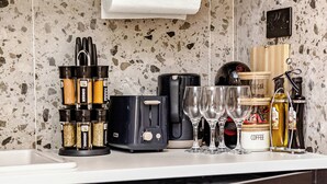 Una cocina con una encimera, dispensador de toallas de papel, cafetera, tostadora, una copa de vino, una botella de aceite de oliva y un estante con especias.